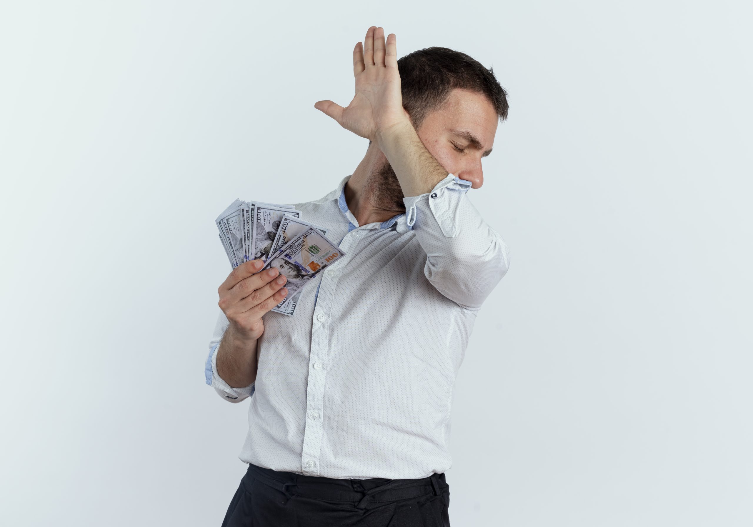 annoyed handsome man holds money and raises hand hiding face looking at side isolated on white background with copy space